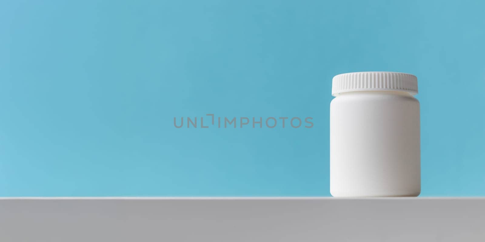 White plastic medicine bottle on a blue background with copy space. Medicine and health concepts include a jar with pills or vitamins. High-quality photo mock-up banner. Healthy Bio Supplements
