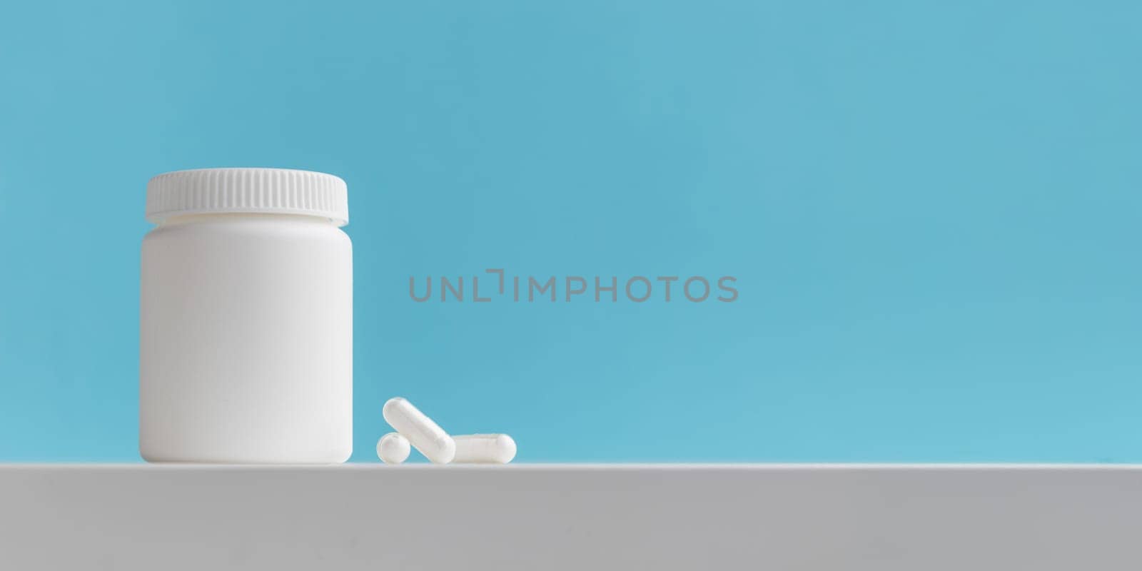 White pills and plastic medicine bottle on a blue background with copy space. Medicine and health concepts include a jar with pills or vitamins. High-quality photo mock-up banner. Healthy Bio Supplements
