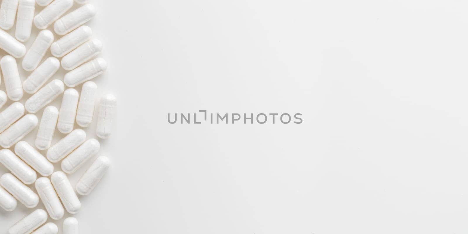Scattered white medicine, pills or capsules on white table. Mock up background from top view with a copy space. Medical, pharmacy and healthcare. High-quality mock-up banner. Healthy Bio Supplements.
