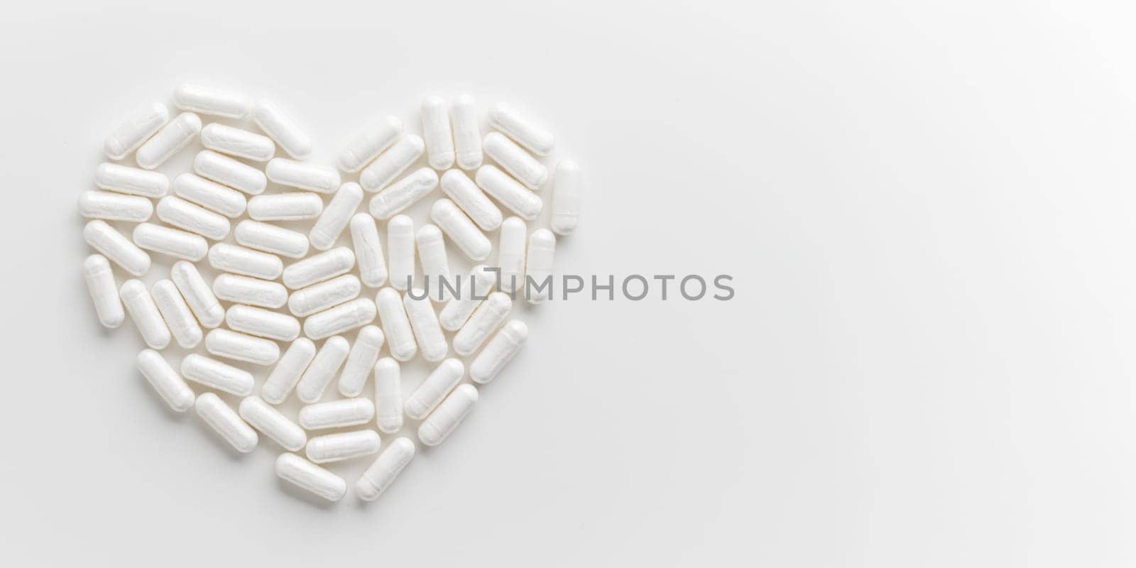 White Pills are arranged in heart shape on white table. Mock up background from top view with a copy space. Medical, pharmacy and healthcare. High-quality photo mock-up banner