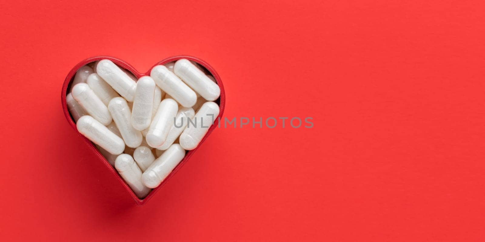 The heart made of white medicine on a red table. Medicinal pills and capsules for health, dietary supplements and vitamin. Mock up background from top view with a copy space.