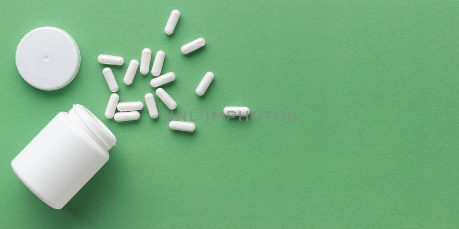 Pharmaceutical medicine capsules with the bottle on green background and copy space for text. Medicine and health concepts include a jar with pills, antibiotic or vitamins. High-quality mock-up banner