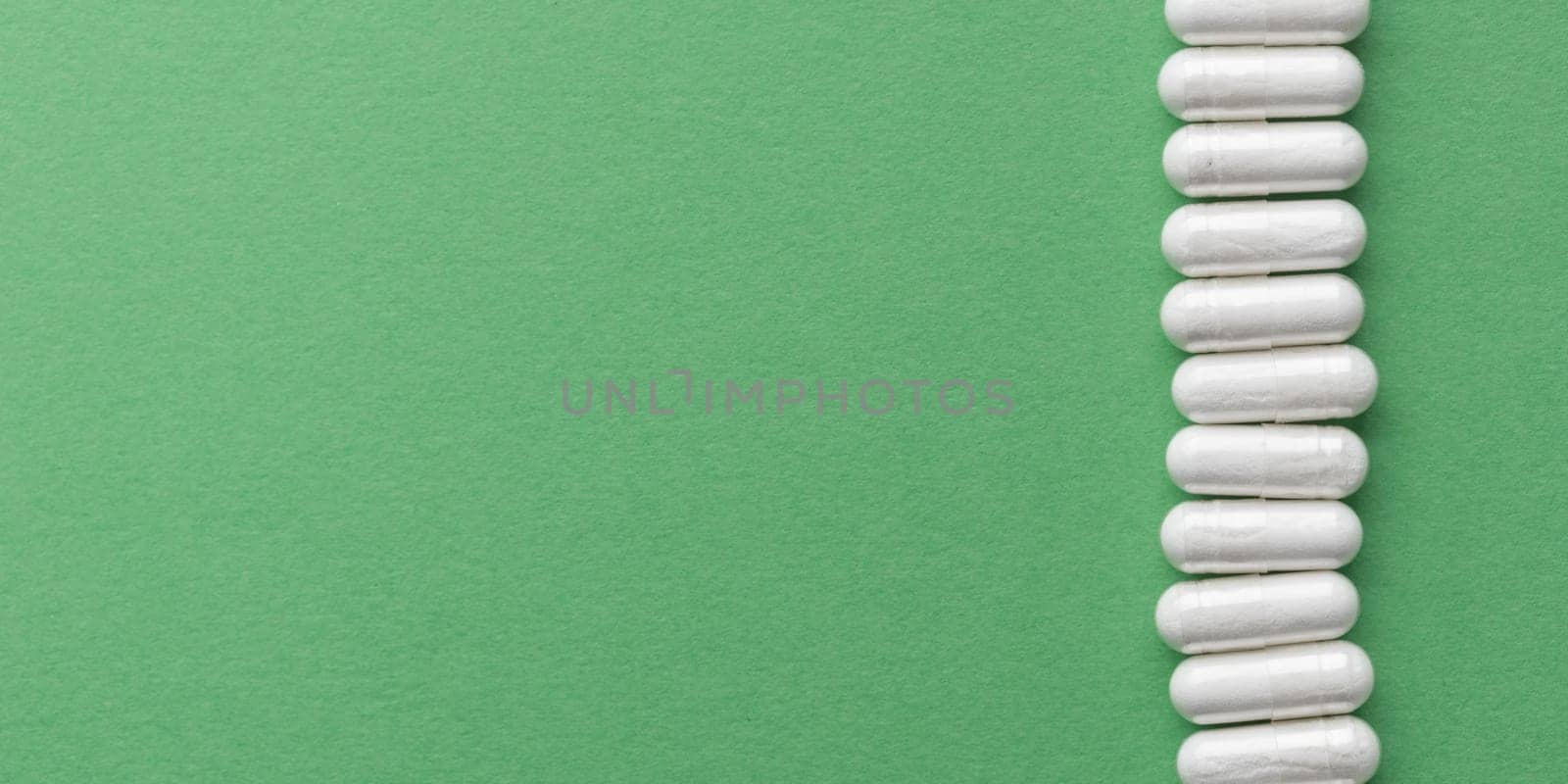 Scattered white medicine, pills or capsules on green table. Mock up background from top view with a copy space. Medical, pharmacy and healthcare. High-quality photo mock-up banner