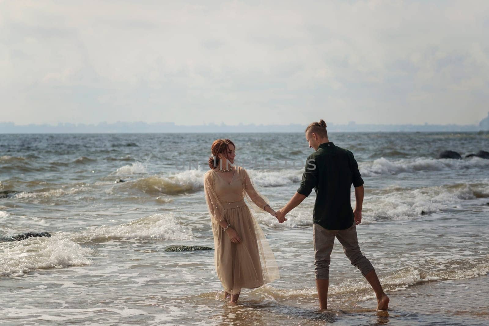 lovers and romantic newlyweds having fun on the seashore. couple running on the water. on a bright sunny day lovers dancing on the sea. girl wearing a beige dress. they barefoot in the sea