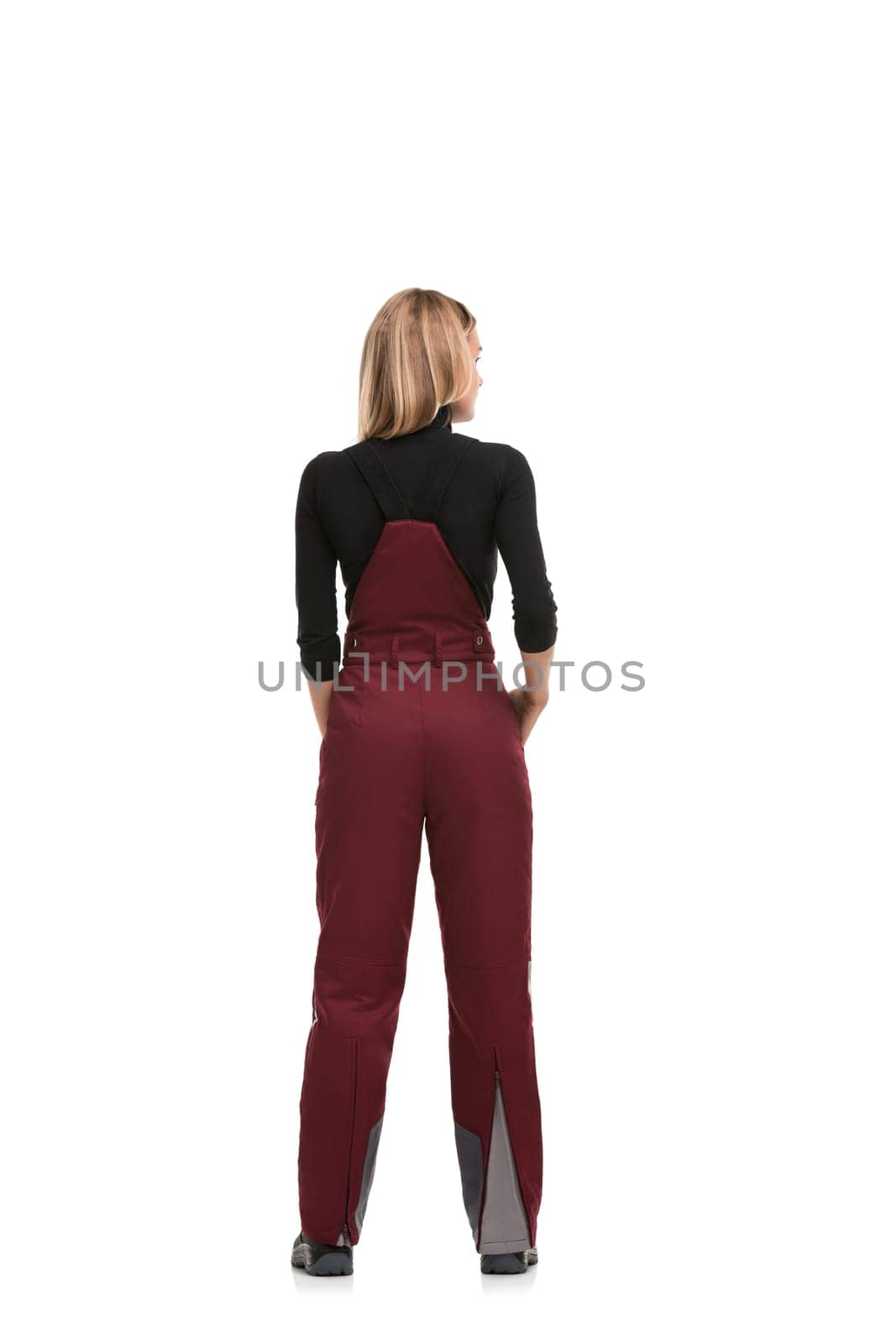 Girl in burgundy working overalls and black long sleeve isolated full-length rearview