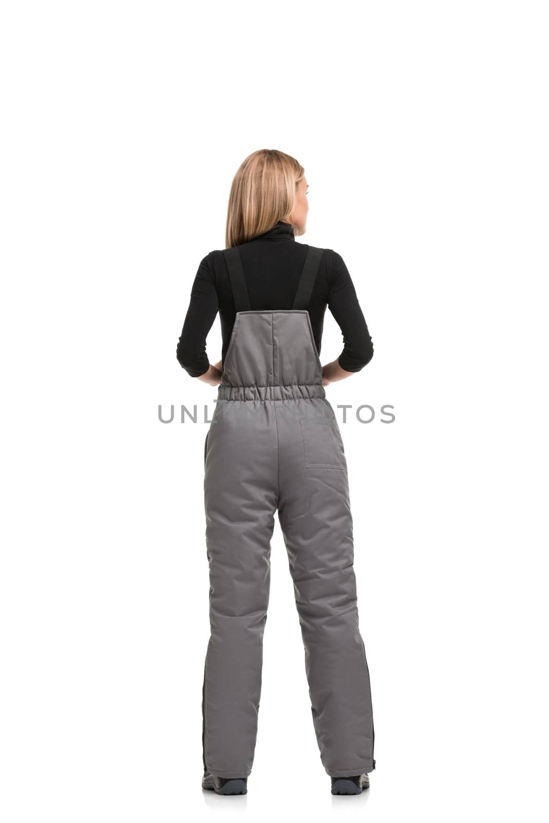 Woman in gray working zipped overalls and black long sleeve isolated full-length rearview