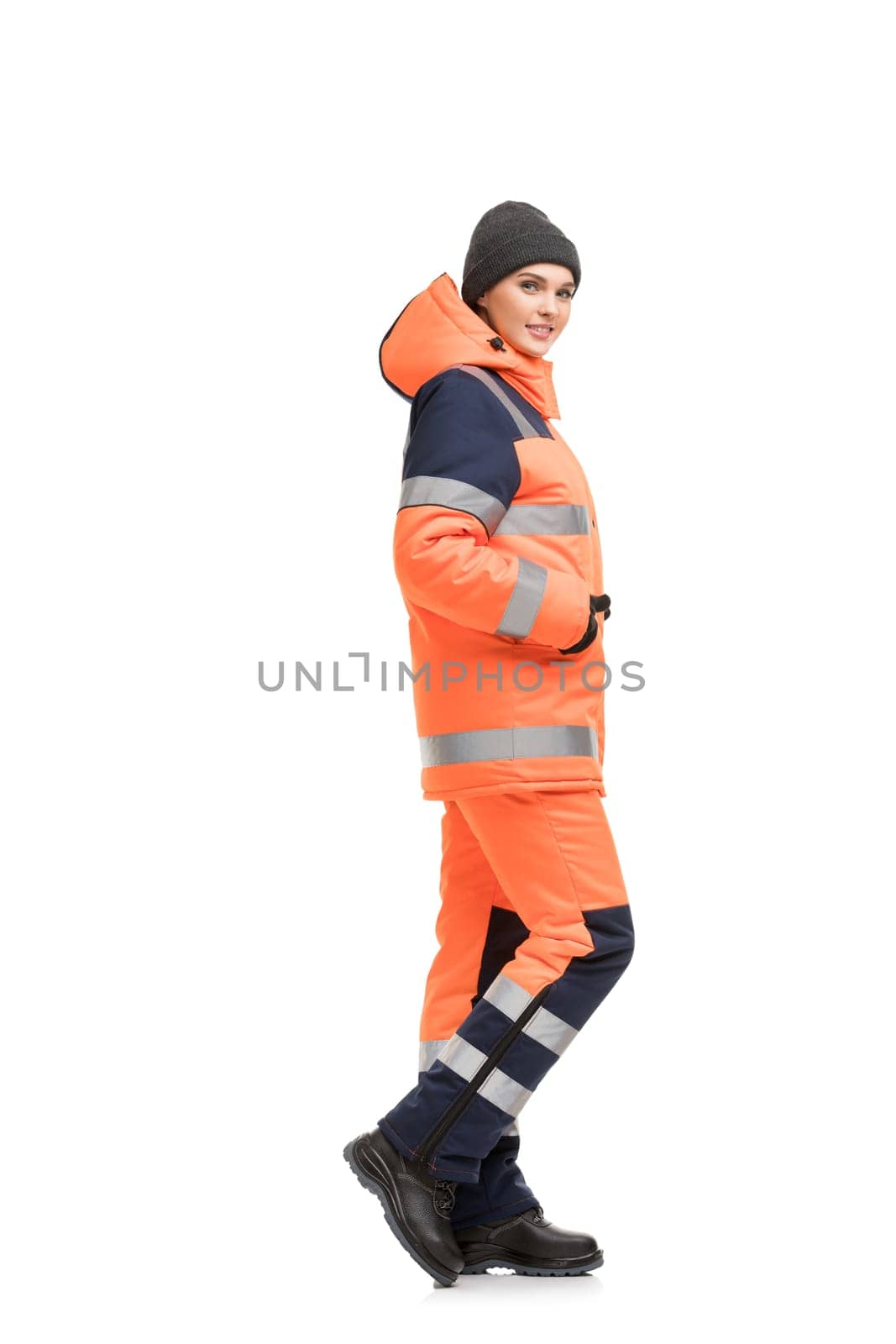 Woman in orange working trousers and jacket with reflective strips and knitted cap isolated full-length profile view