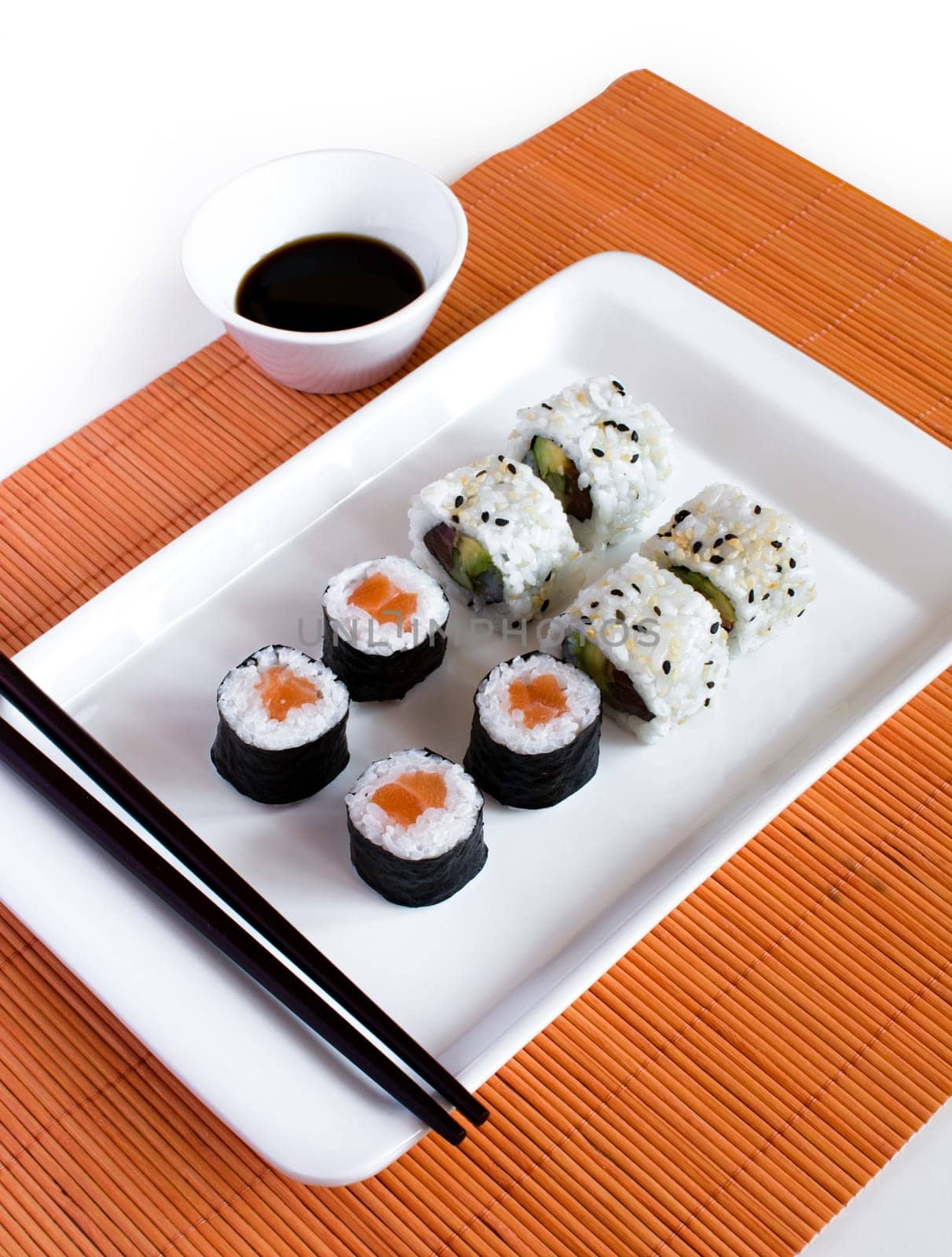 Delicious sushi rolls on white plate with chopsticks