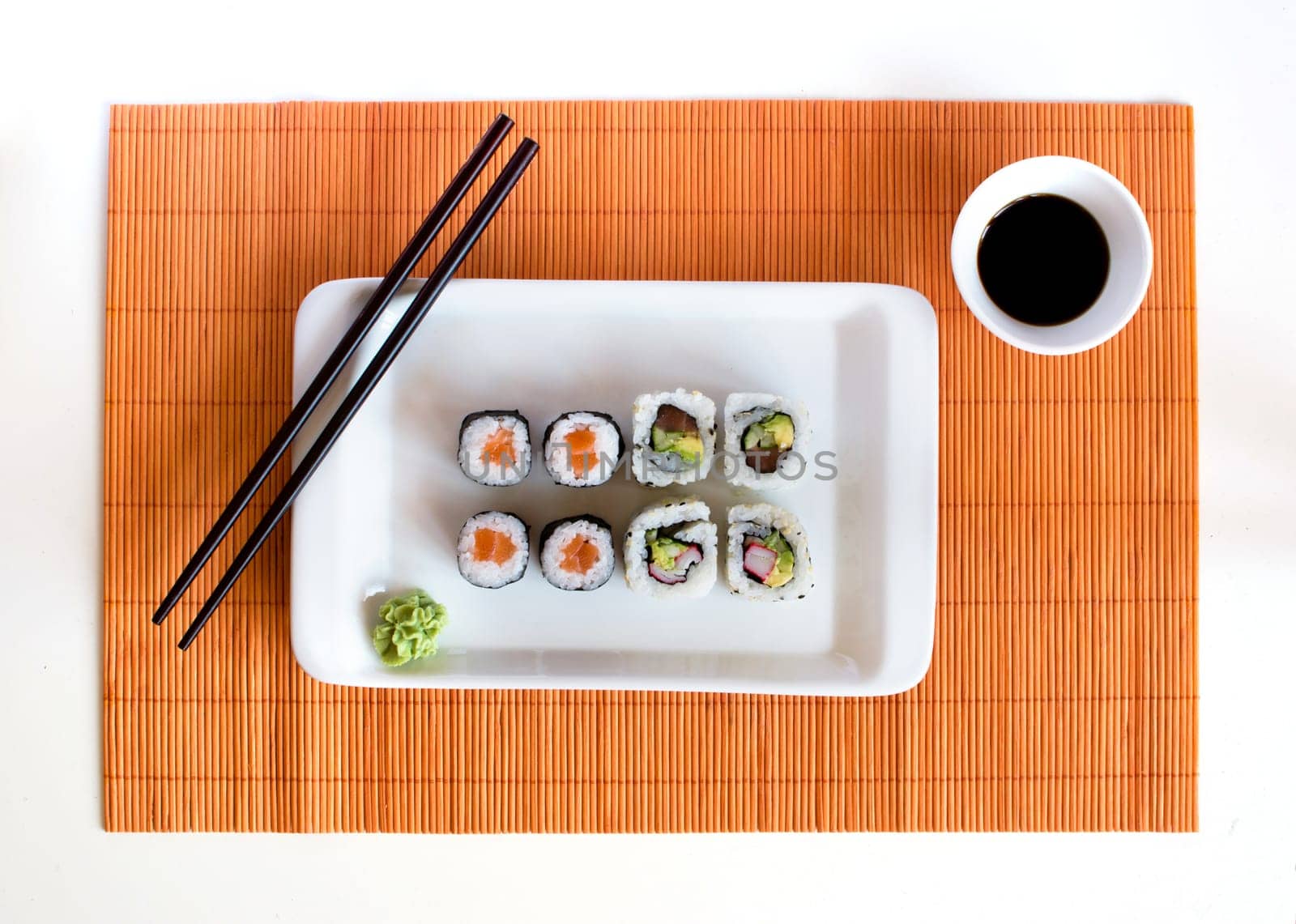 Delicious sushi rolls on white plate with chopsticks