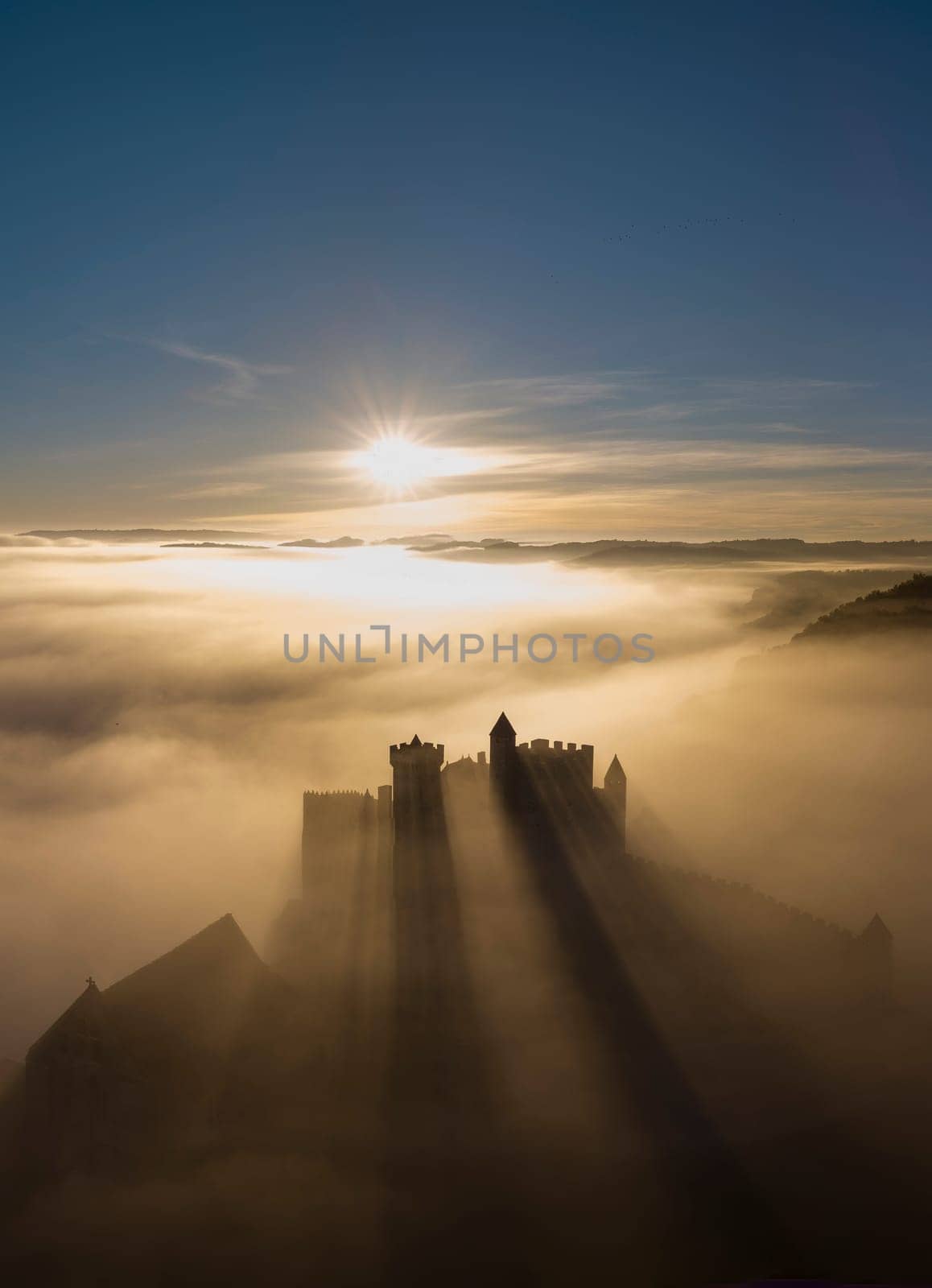 Chateau de Beynac stands majestically as the sun rises, casting long shadows through the mist, showcasing the enchanting beauty of Dordogne's landscape.