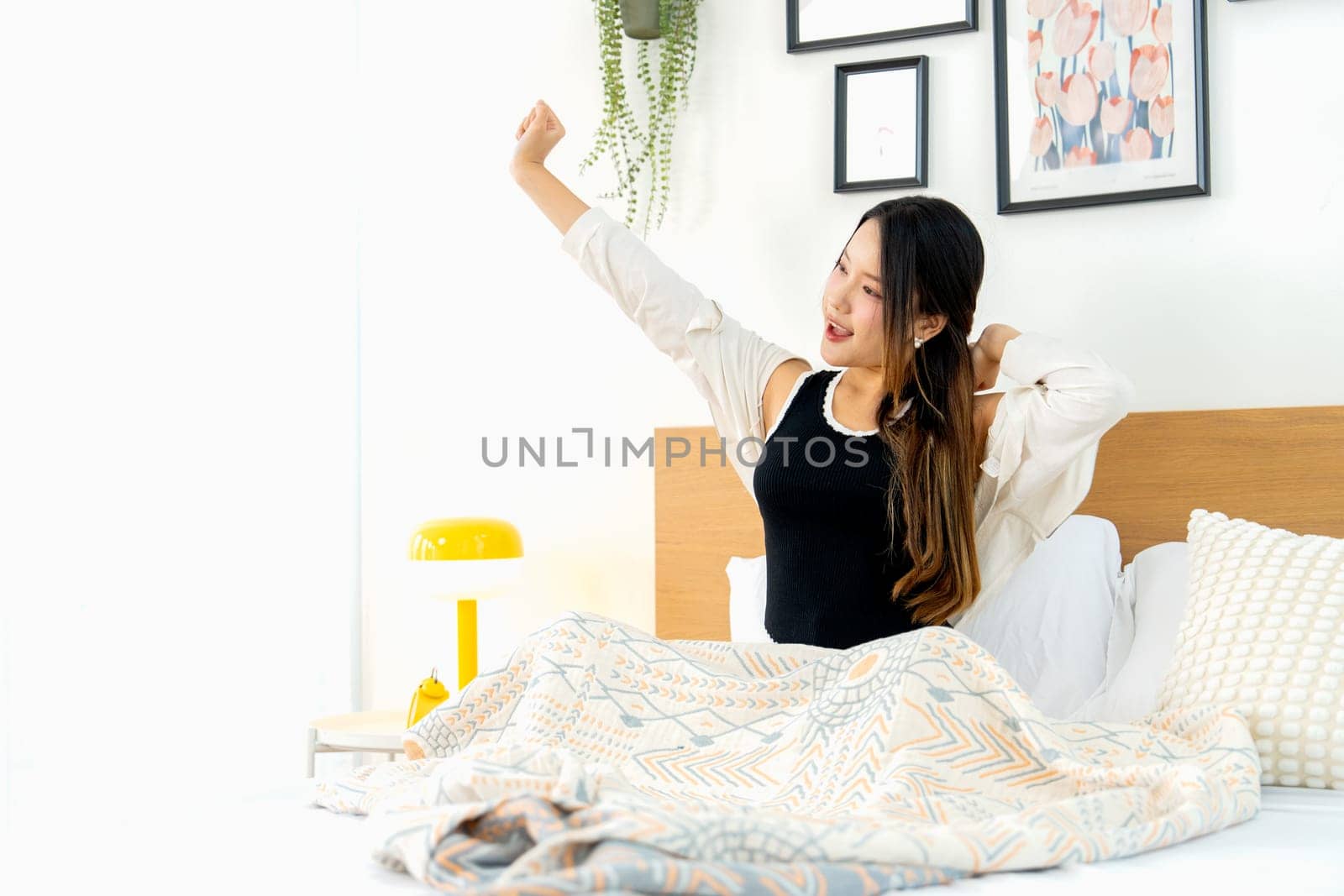 Beautiful young Asian woman lean on bed with stretch lazily and relax in bedroom with day light.