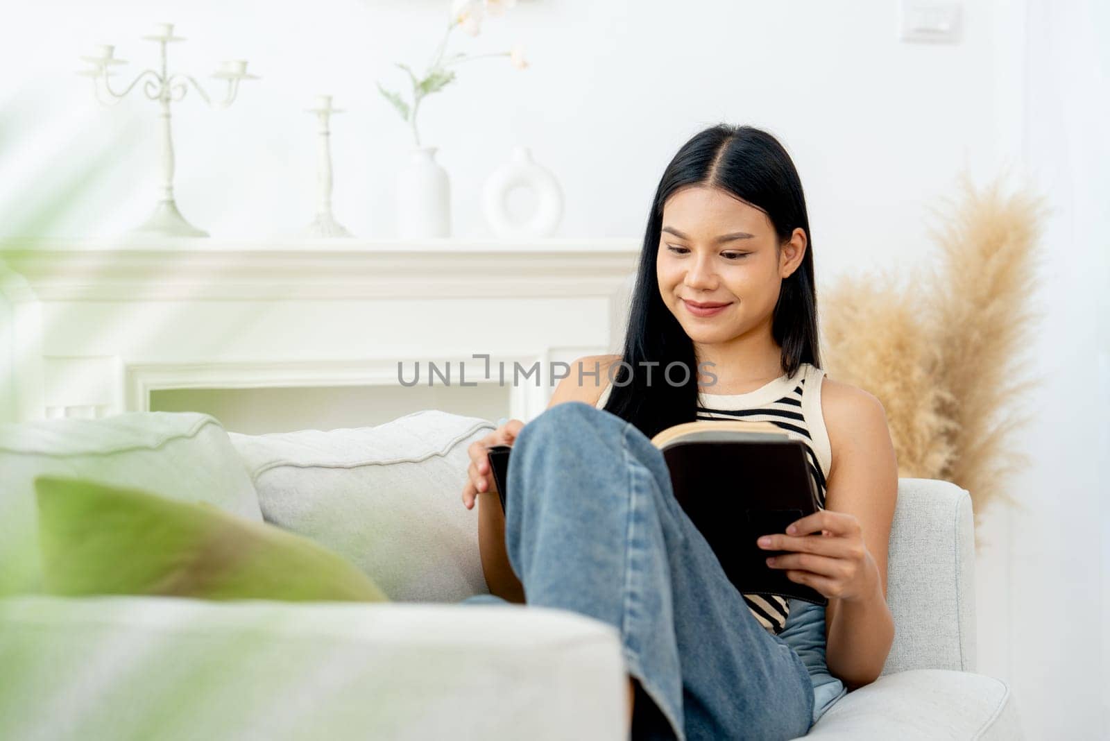 Front view and portrait of beautiful Asian woman lean on sofa also enjoy to read the book and happiness with day light.