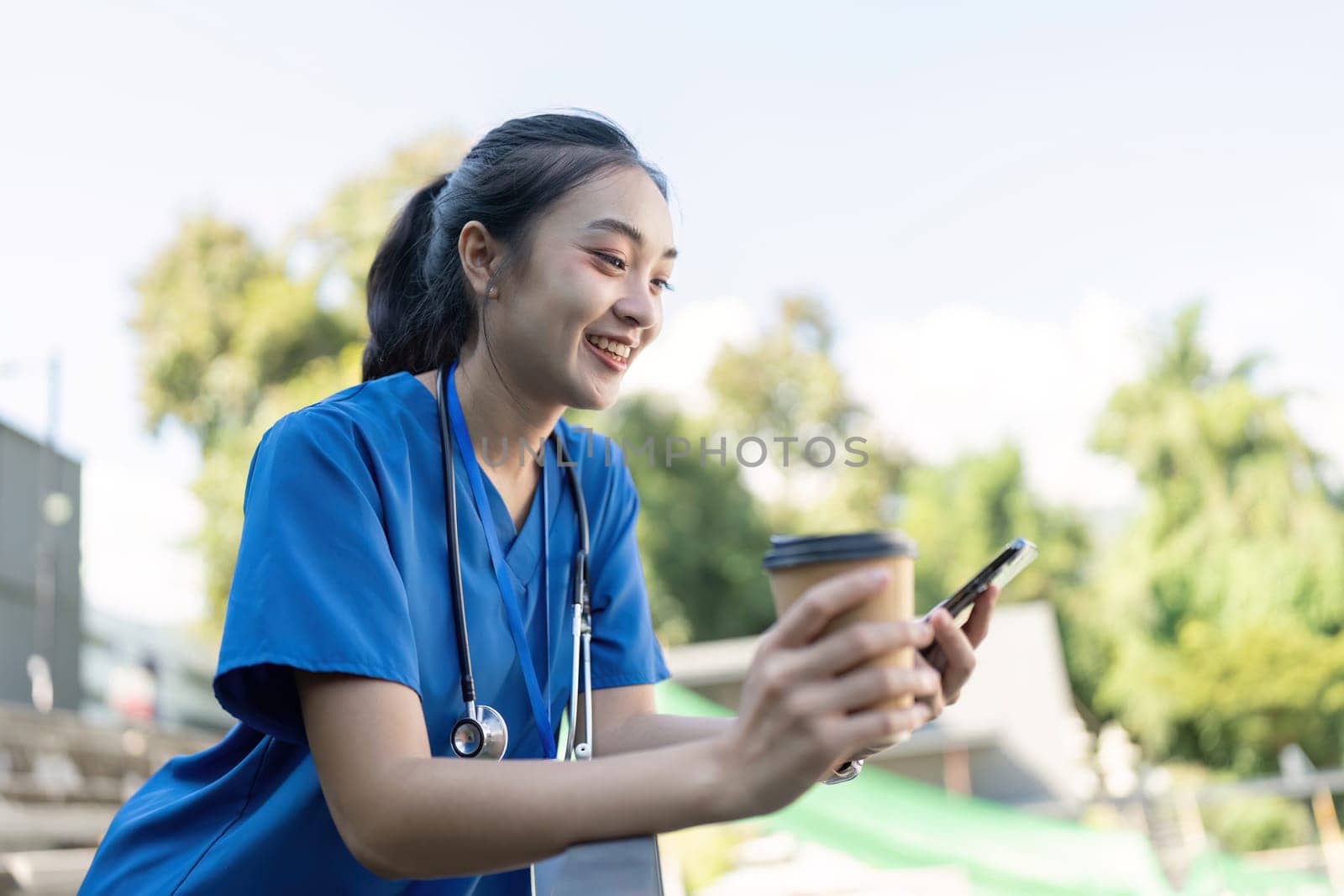 Joyful nurse enjoying the outdoors, holding a coffee and checking her phone, embracing a moment of relaxation in between shifts.