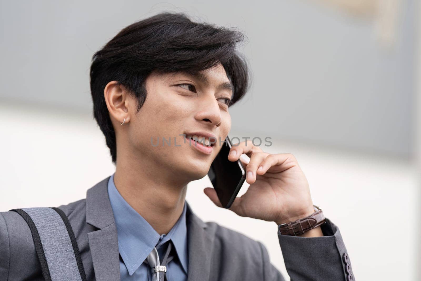 A confident young Asian businessman engaged in a phone conversation, showcasing professionalism and style in a work setting.