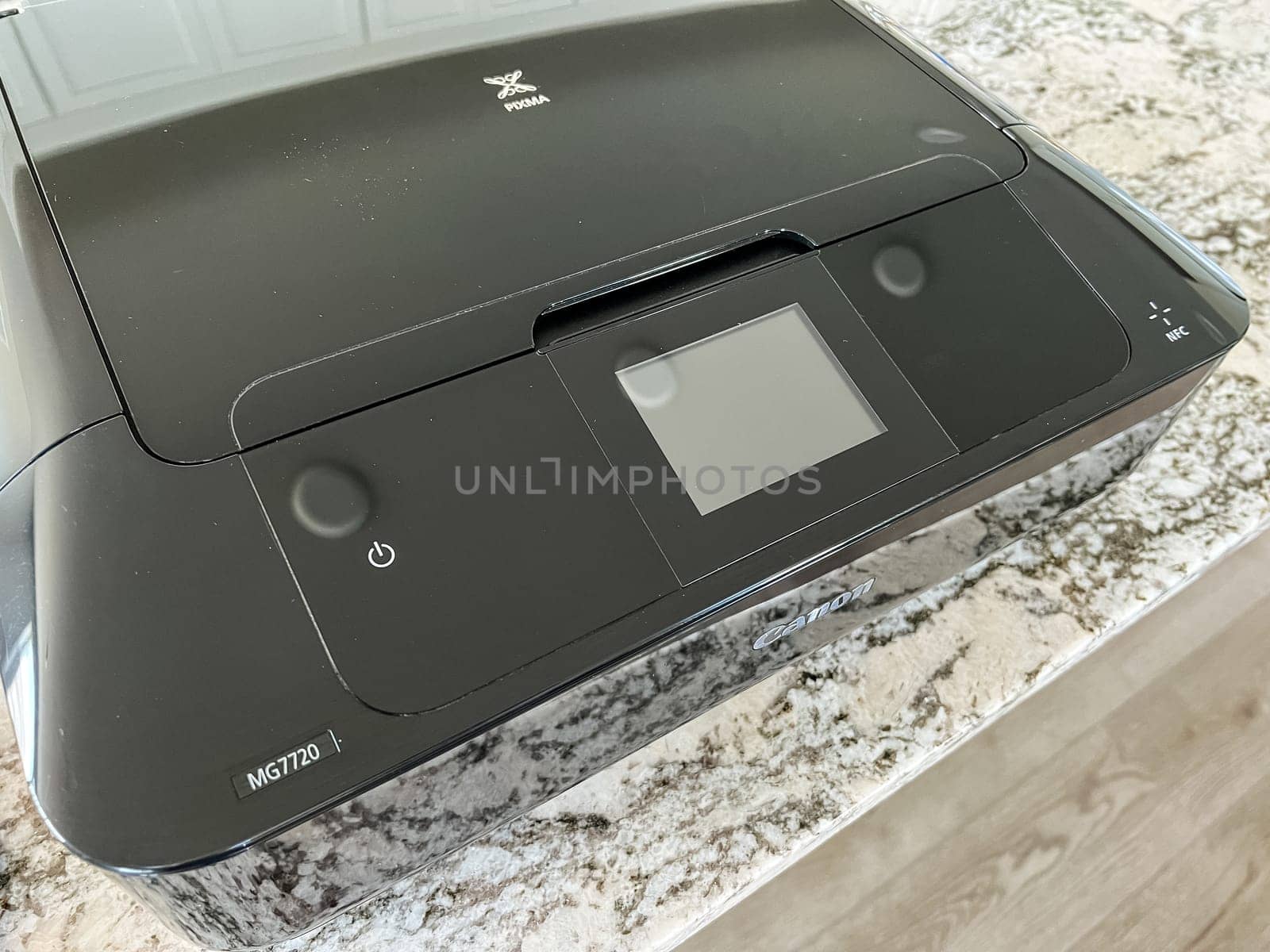 Castle Rock, Colorado, USA-May 8, 2023-A close-up image of a Canon printer placed on a granite countertop. The printer black glossy exterior prominently displays the Canon logo, reflecting light. The countertop beneath showcases a modern kitchen setting, blending functionality with sleek design.