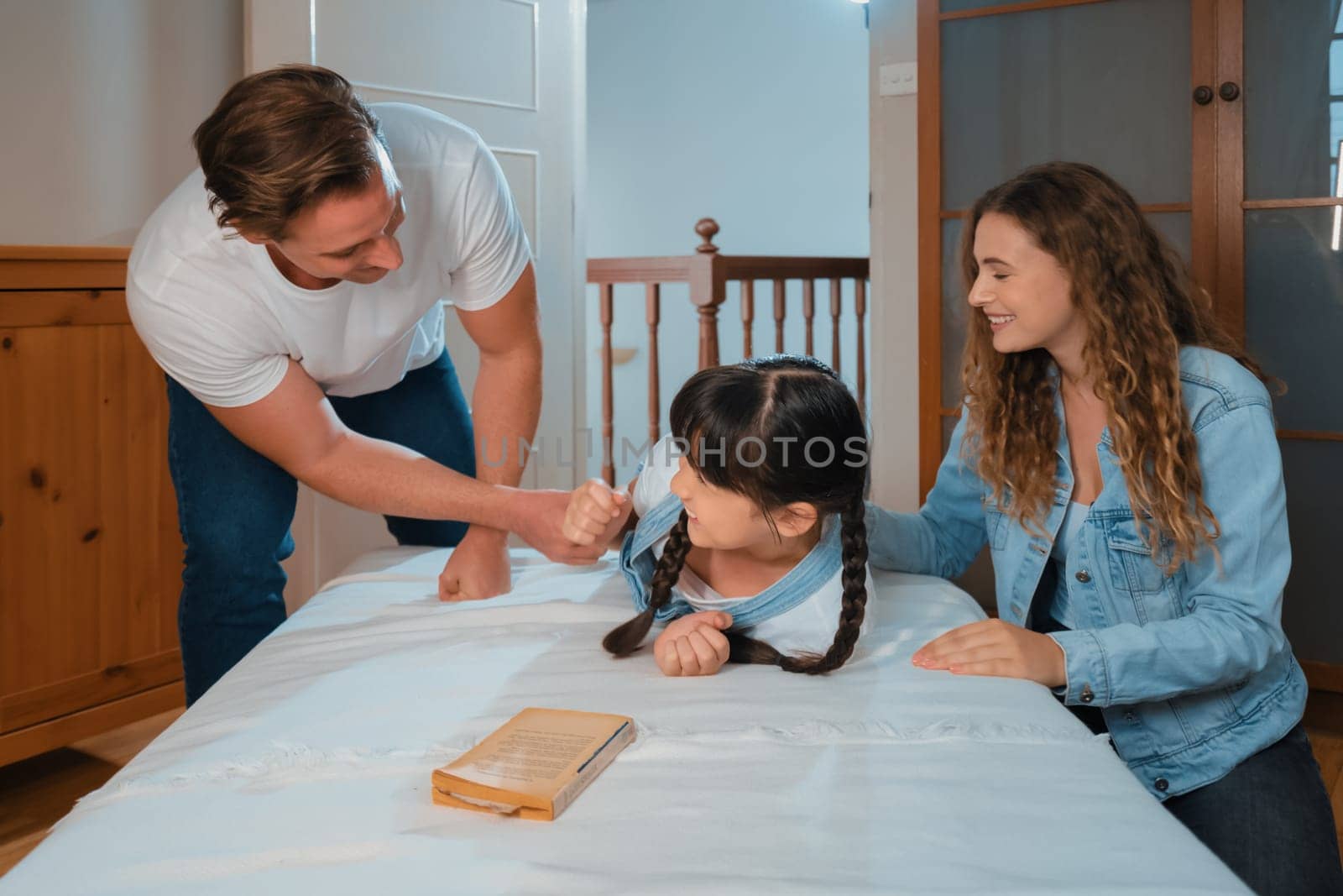 Happy modern family wakes up their little girl on the weekend with playful tickle expressing their love and affection for their young daughter, laughing and smiling together. Synchronos