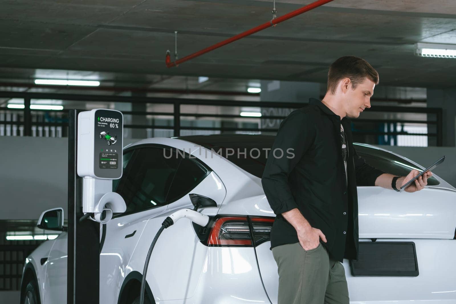 Young man travel with EV electric car to shopping center parking lot charging in downtown city showing urban sustainability lifestyle by green clean rechargeable energy of electric vehicle innards