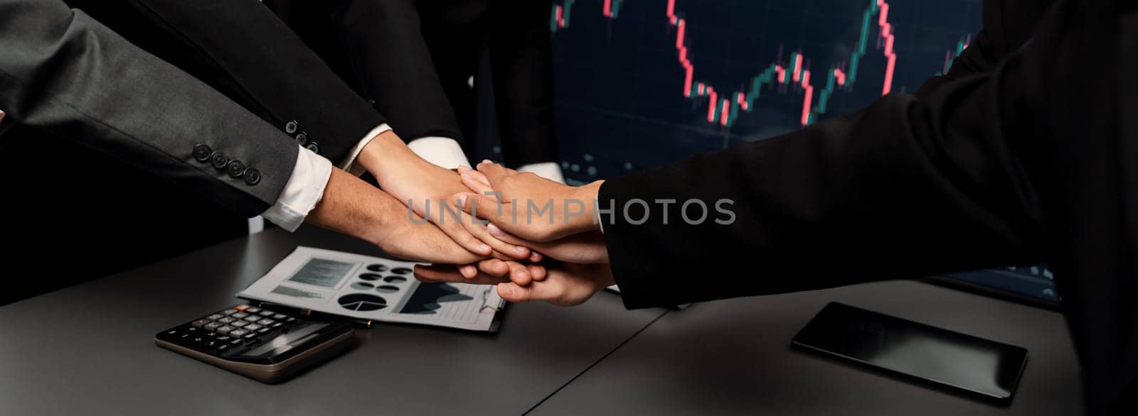 Stock investor put hand stack together over meeting table as synergy teamwork after made successful financial data analysis on stock graph and strategic planning for stock trading. Trailblazing