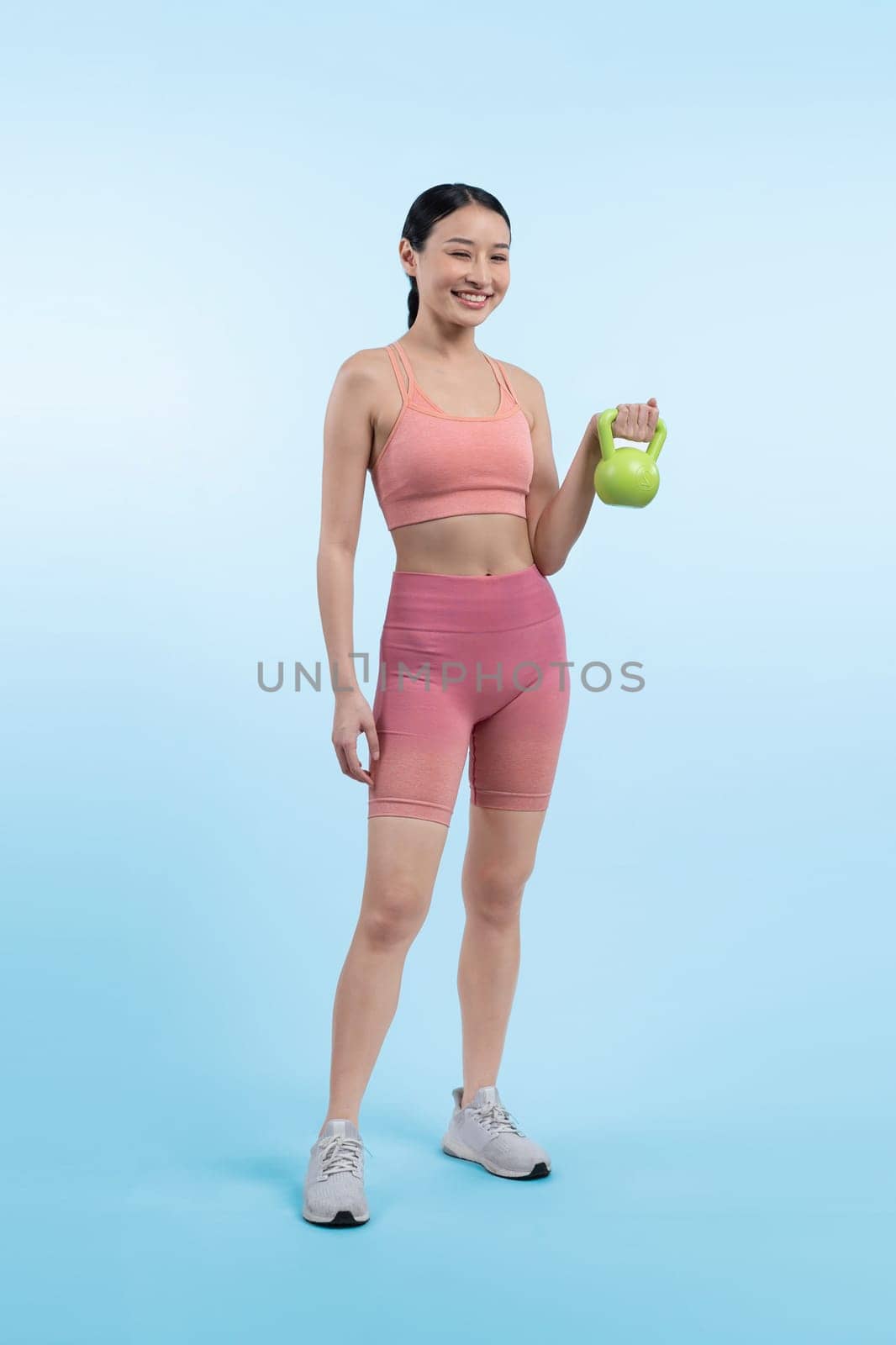 Vigorous energetic woman doing kettlebell weight lifting exercise on isolated background. Young athletic asian woman strength and endurance training session as body workout routine.