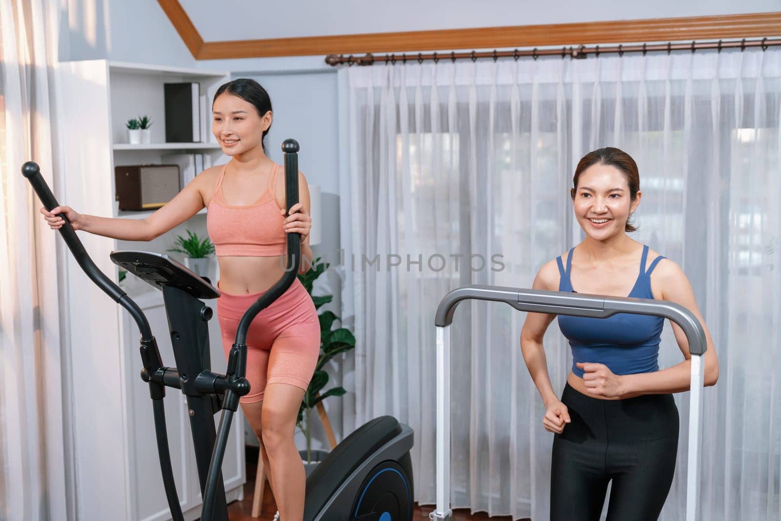 Energetic and strong athletic asian woman running on elliptical running machine at home with workout buddy or trainer. Pursuit of fit physique and commitment to healthy lifestyle. Vigorous