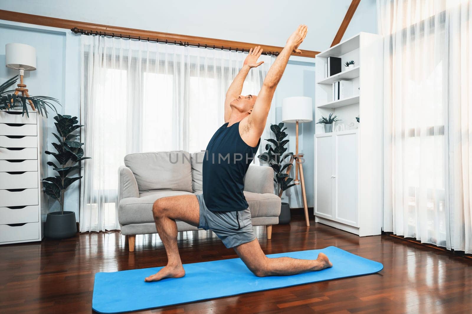 Happy active senior man in sportswear being doing yoga posture on exercising mat at home. Healthy senior pensioner lifestyle with yoga exercise. Clout