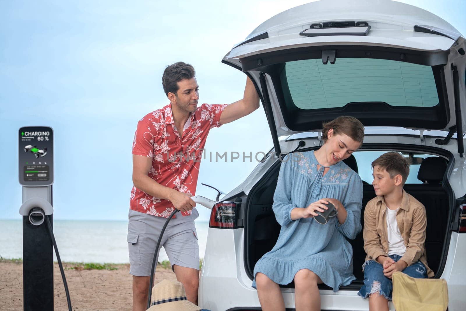 Family vacation trip traveling by the beach with electric car, lovely family sit on the trunk, charging EV car battery with green and sustainable energy. Family travel and eco-friendly car. Perpetual