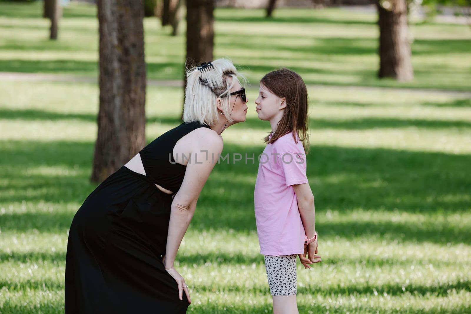Girl kisses mother in spring or summer park. Family relaxing outdoors. Mothers day. Close up.
