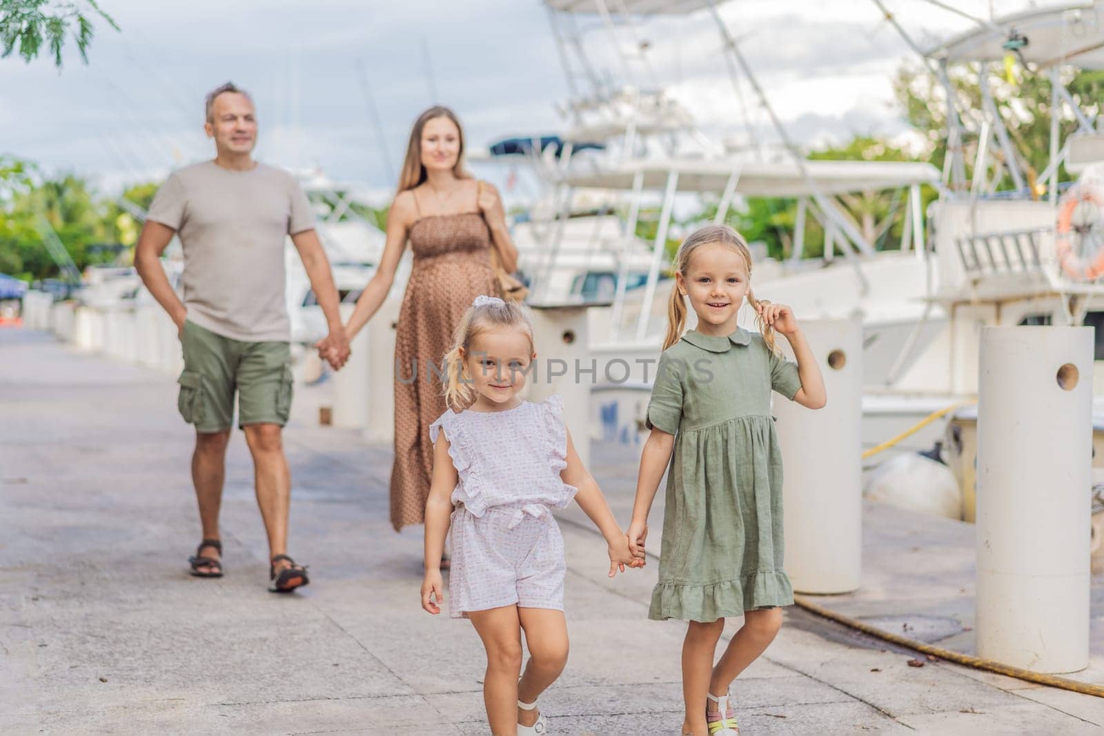 A happy, mature couple over 40 with their two daughters enjoying a leisurely walk on the waterfront, their joy evident as they embrace the journey of pregnancy later in life by galitskaya