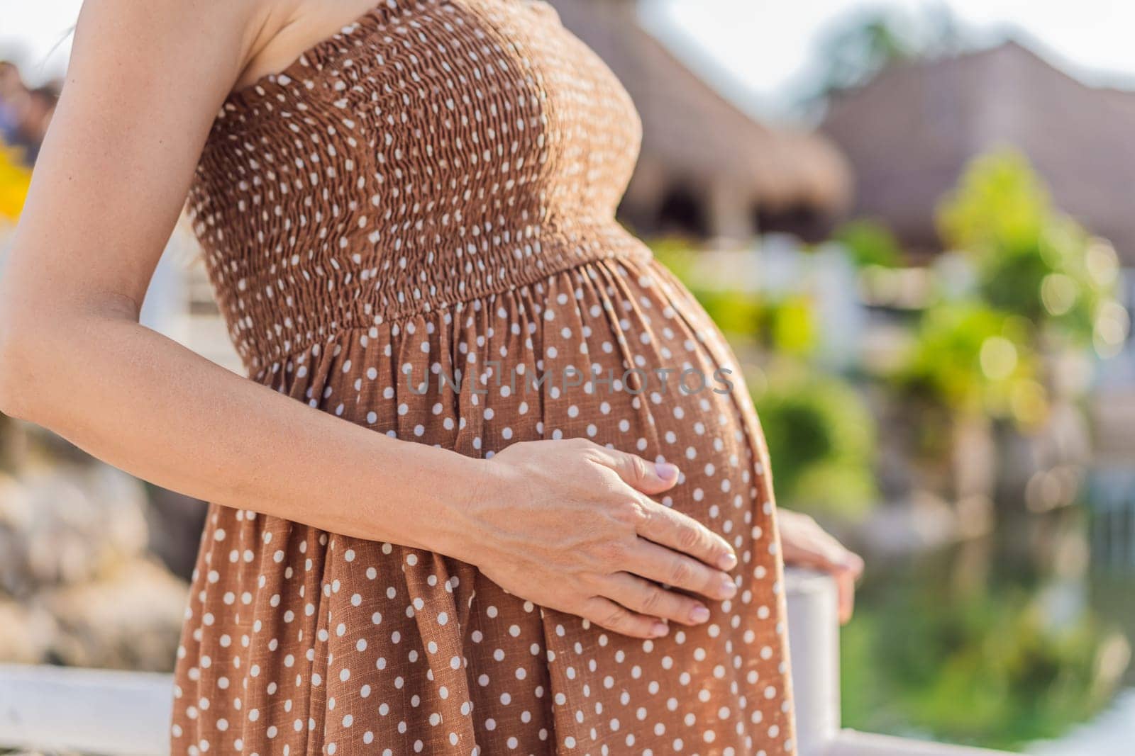 Pregnant woman hugging her tummy standing outdoors surrounded by nature. Pregnancy, expectation, motherhood concept by galitskaya