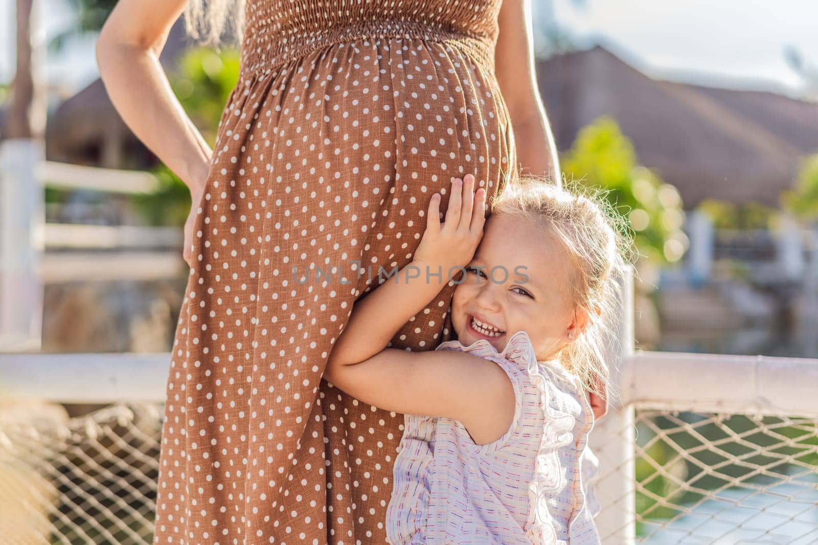 A heartwarming moment captured as a daughter lovingly embraces her mother's pregnant belly, sharing in the excitement and anticipation of a new family member.