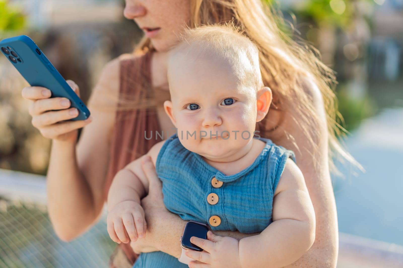 Mom holds her adorable baby while holding a smartphone.