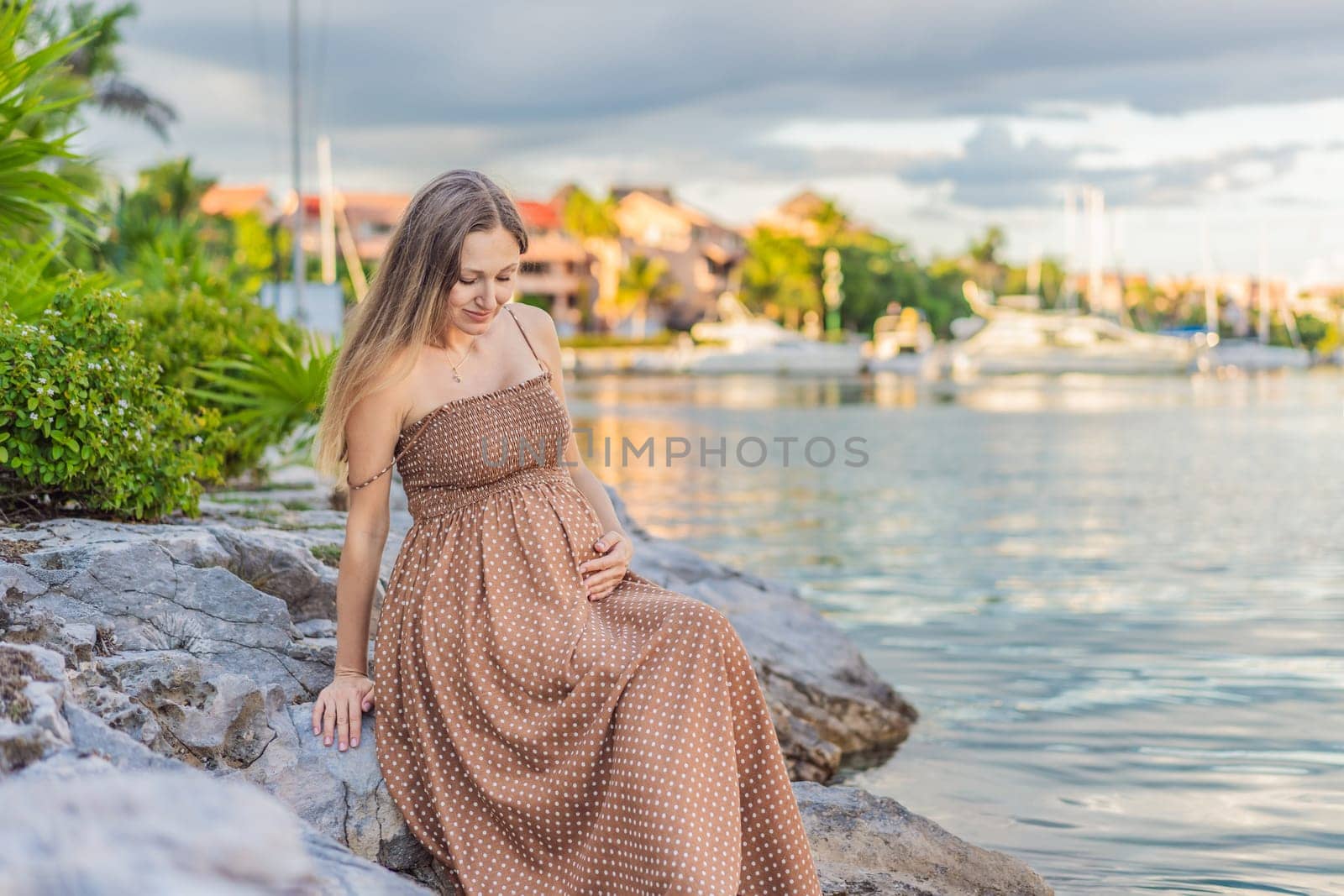 Pregnant woman hugging her tummy standing outdoors surrounded by nature. Pregnancy, expectation, motherhood concept by galitskaya
