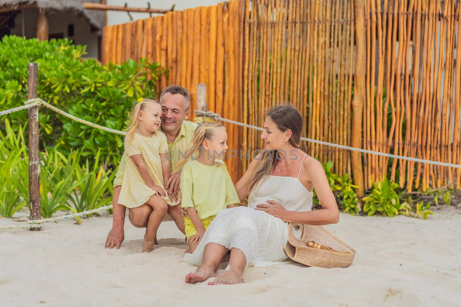 A joyful family, two girls, dad, and a pregnant mom, bask in tropical beach bliss, celebrating a radiant pregnancy amidst paradise by galitskaya