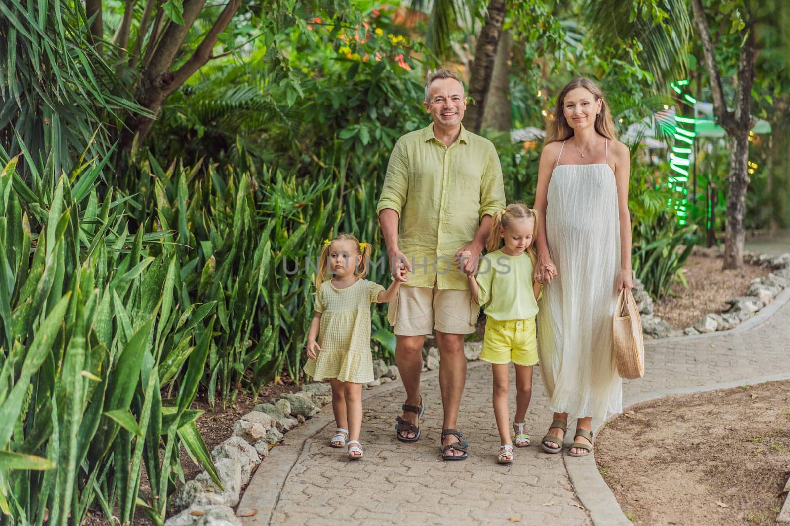 A joyful family, two girls, dad, and a pregnant mom, bask in tropical resort, celebrating a radiant pregnancy amidst paradise.
