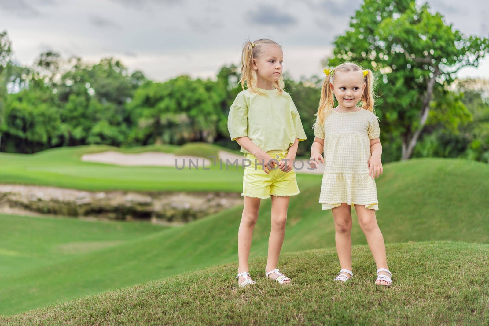 Two adorable sisters share a heartwarming moment on a green lawn, their sisterly bond radiating love and joy in the great outdoors.