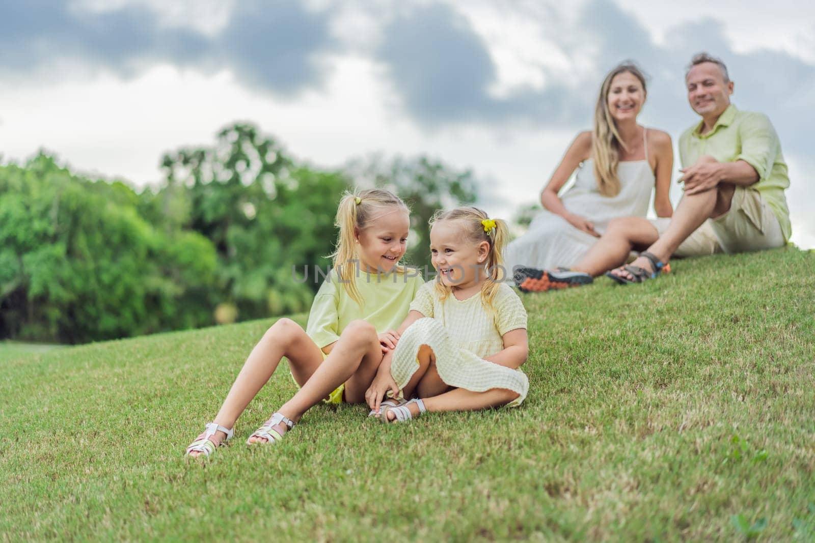A happy family, two girls, dad, and a pregnant mom, enjoys quality time together on a lush green lawn, creating cherished memories of togetherness.