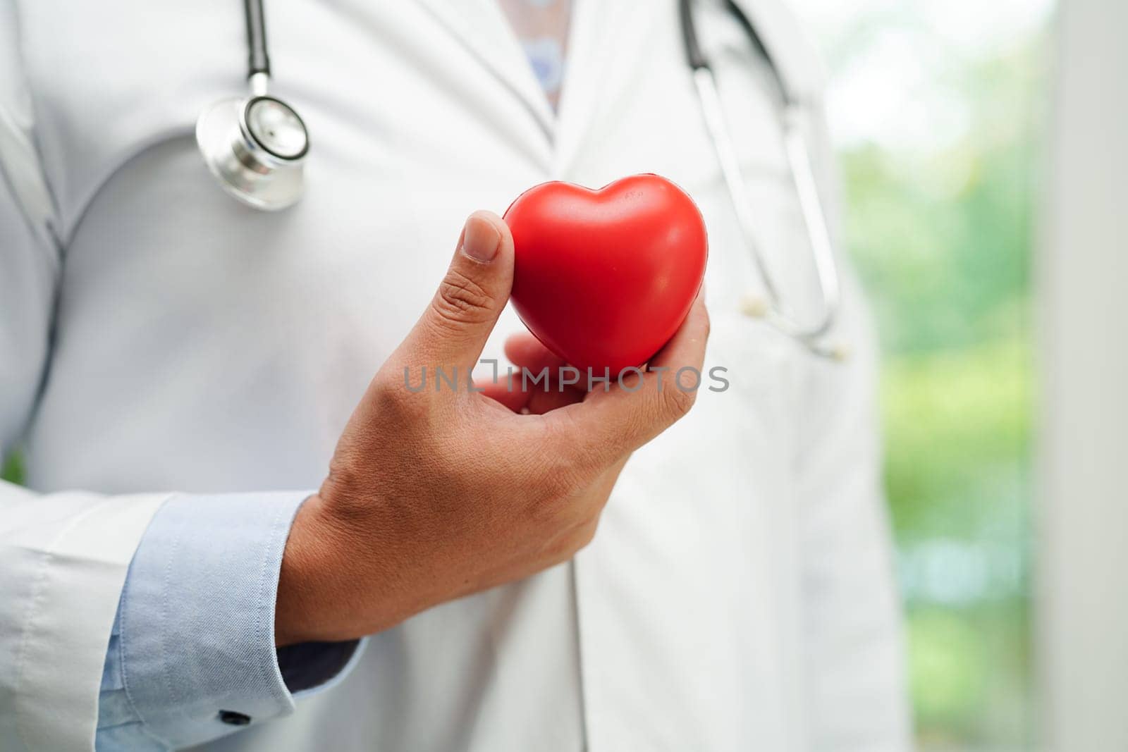 Asian woman doctor holding red heart for health in hospital.