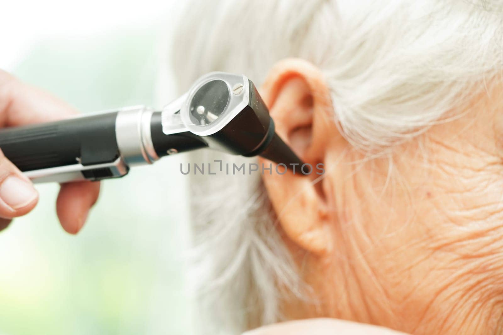 Otolaryngologist or ENT physician doctor examining senior patient ear with otoscope, hearing loss problem.