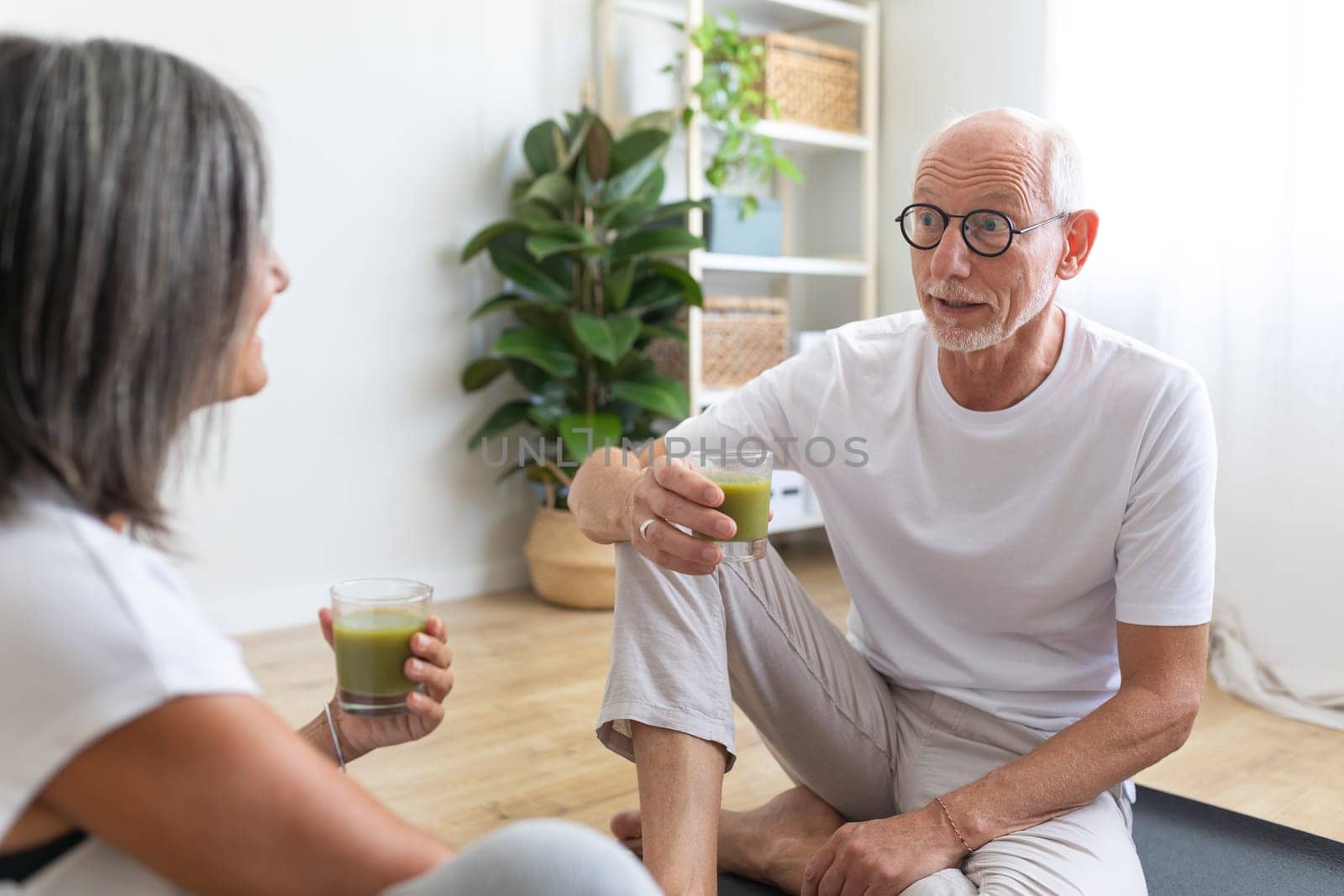 Mature caucasian man drinking healthy green juice after exercising with wife at home. Healthy and active lifestyle concept.