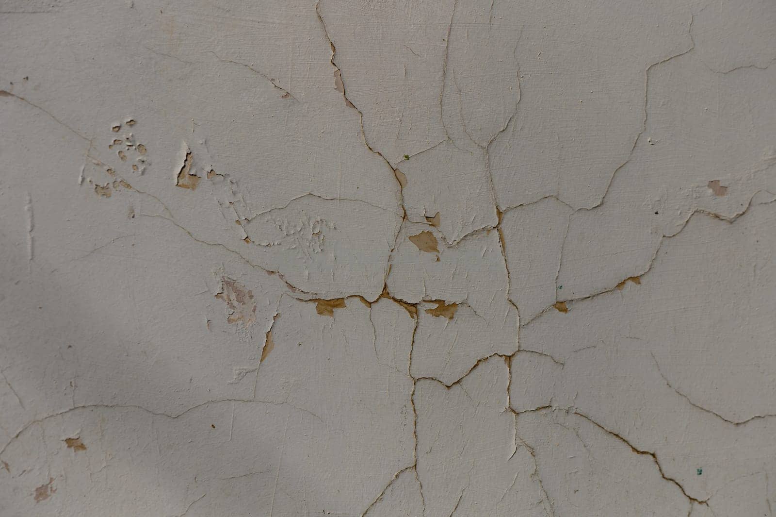 Fissures snake across peeling plaster, showcasing the passage of time in an old, forgotten structure.