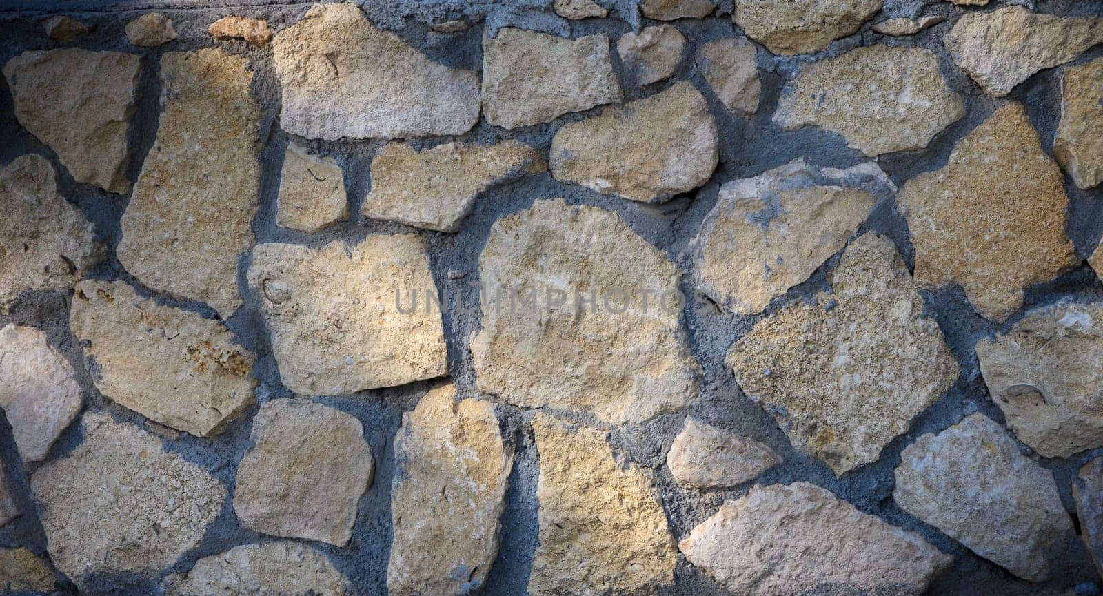Roughly shaped stones blend harmoniously in a textured wall illuminated by warm afternoon rays.