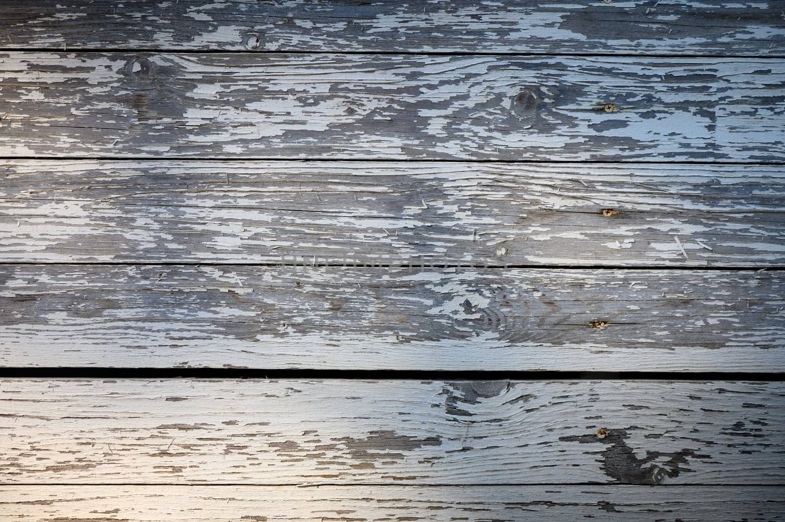 Sunlight casts a gentle glow on old wooden planks, showcasing their texture and history in an outdoor space.