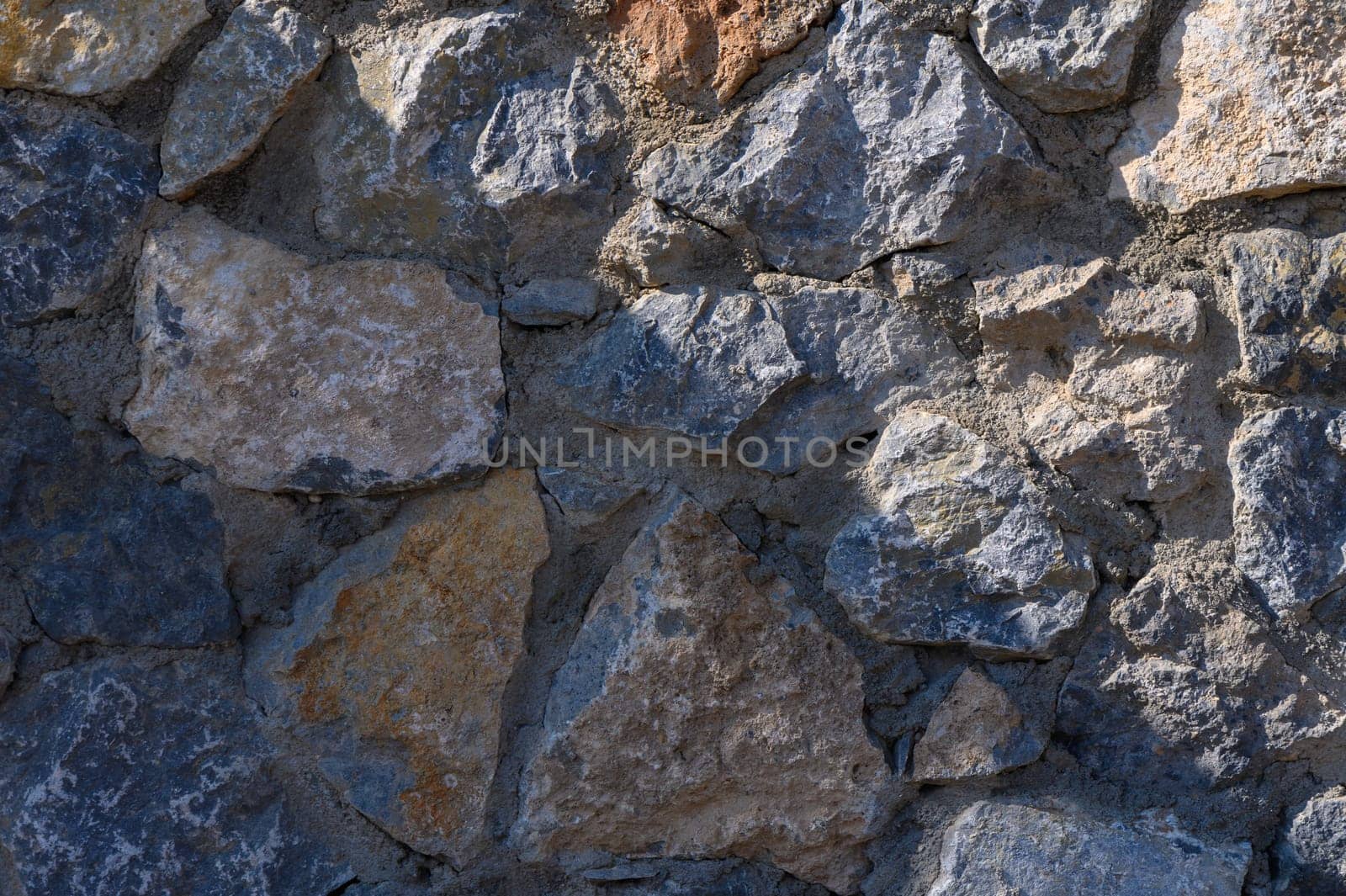 Sunlight reveals the rich textures and colors of a weathered stone wall, showcasing nature's architectural artistry.
