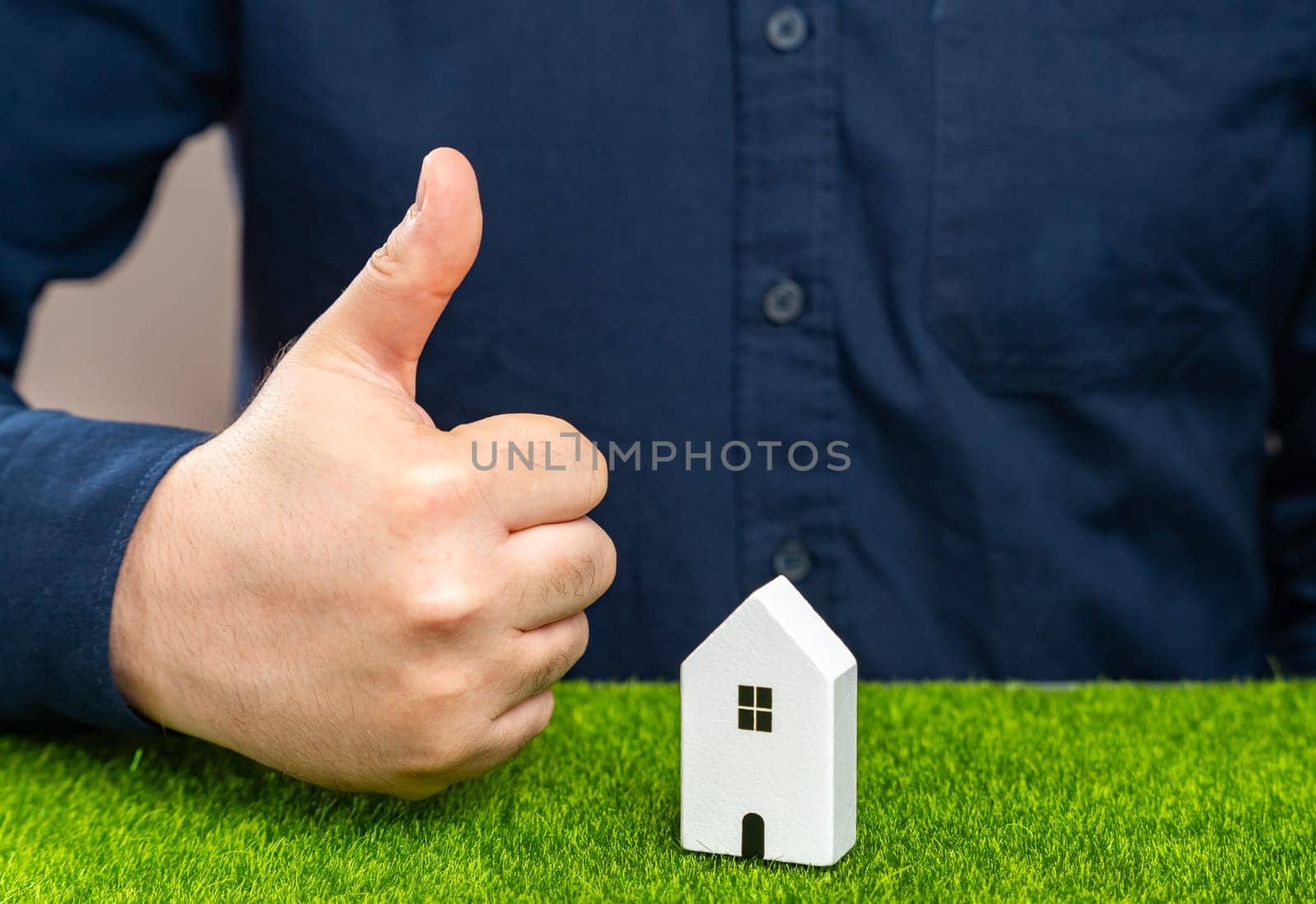 A man shows a thumbs up near a house. Successful real estate investment. Completion of a favorable deal. Approval of a mortgage or loan, making the purchase or renovation possible. Approves condition