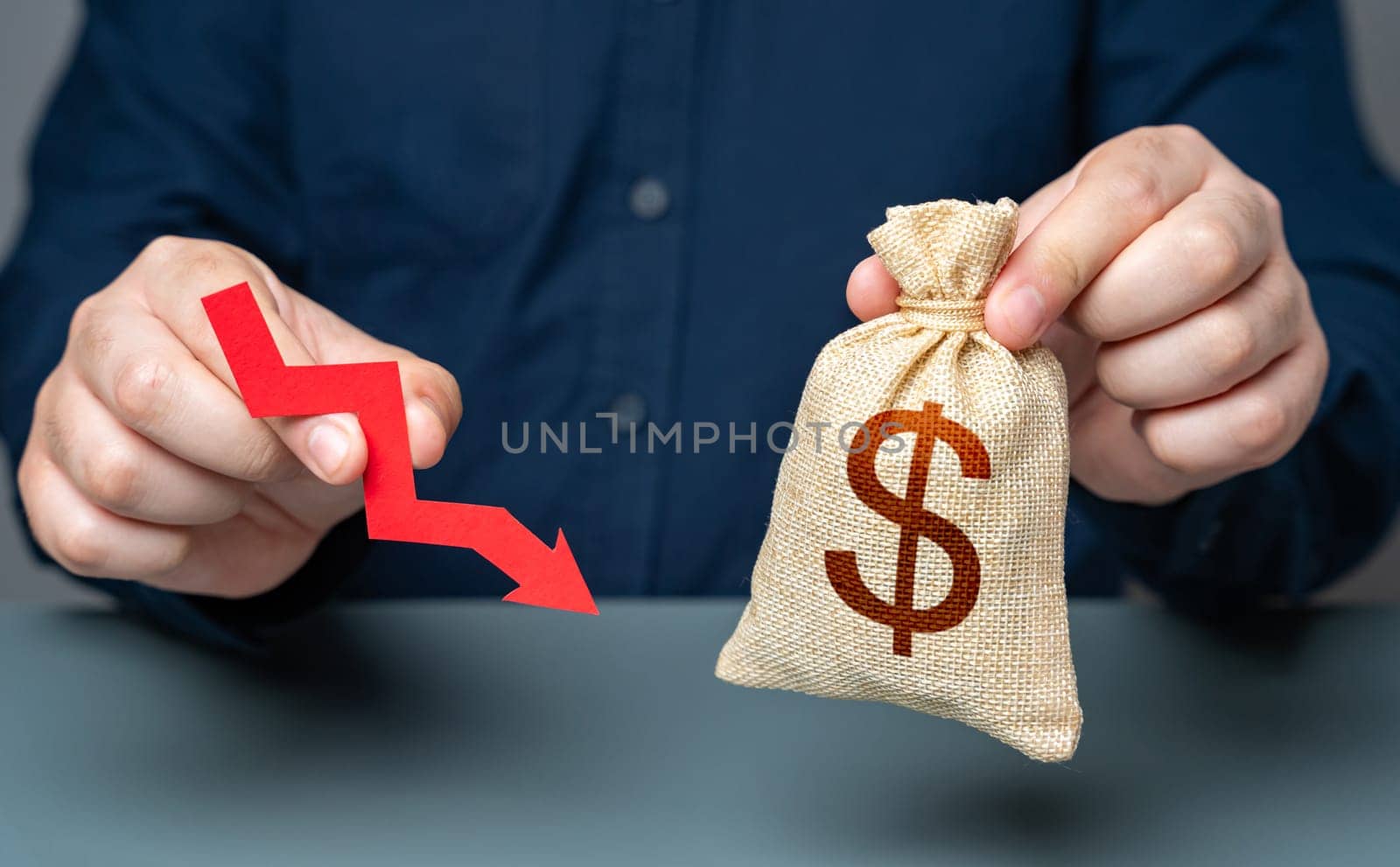 A man holds a red arrow pointing down near a dollar money bag. Financial difficulties, losses and reduced profitability. Economic downturn. Salary cuts. Financial stress. Devaluation of currency