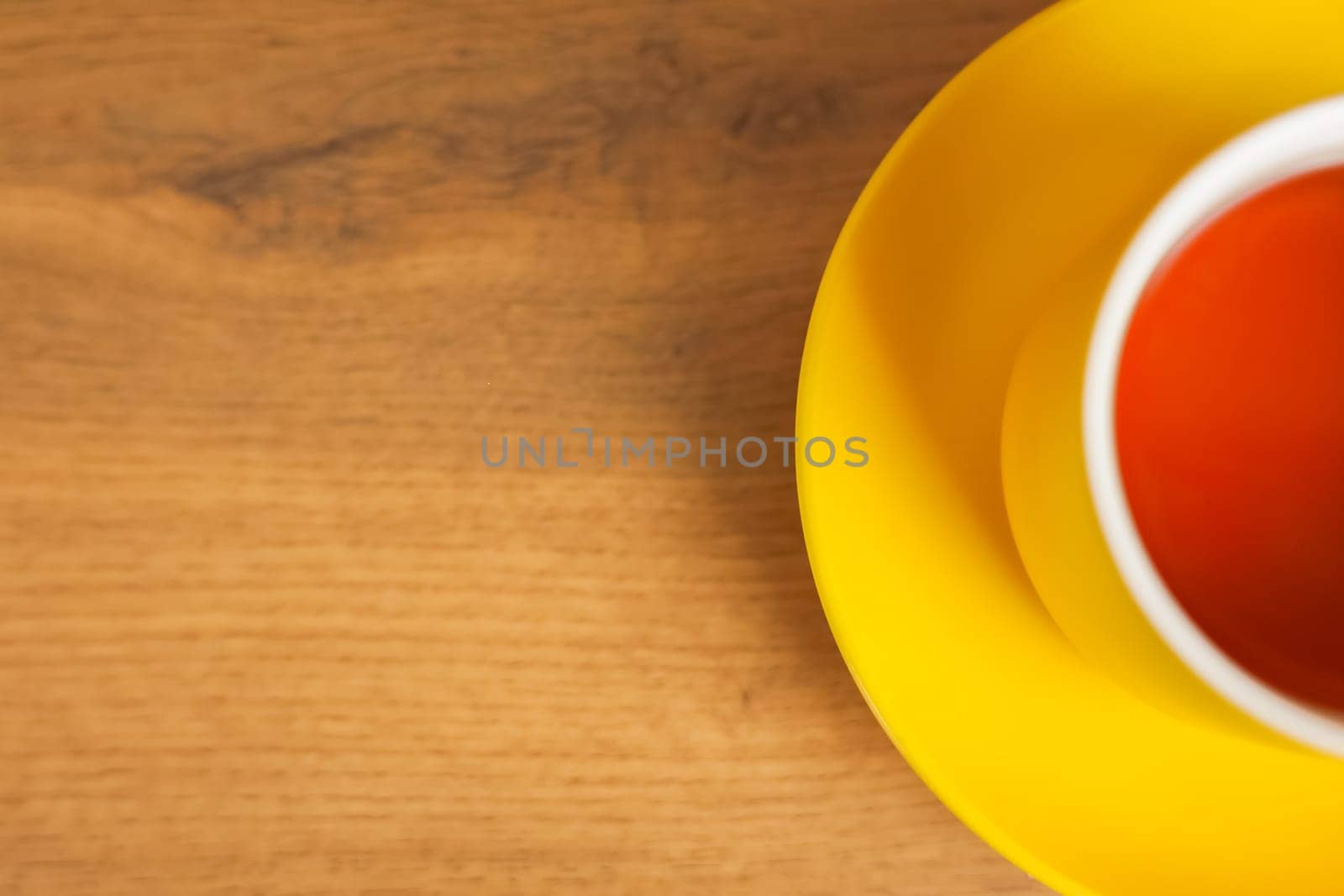 A yellow cup and saucer stands on a wooden background with black tea poured, half of a mug with space for text is visible. The concept of tea drinking, tea tradition, break. High quality photo