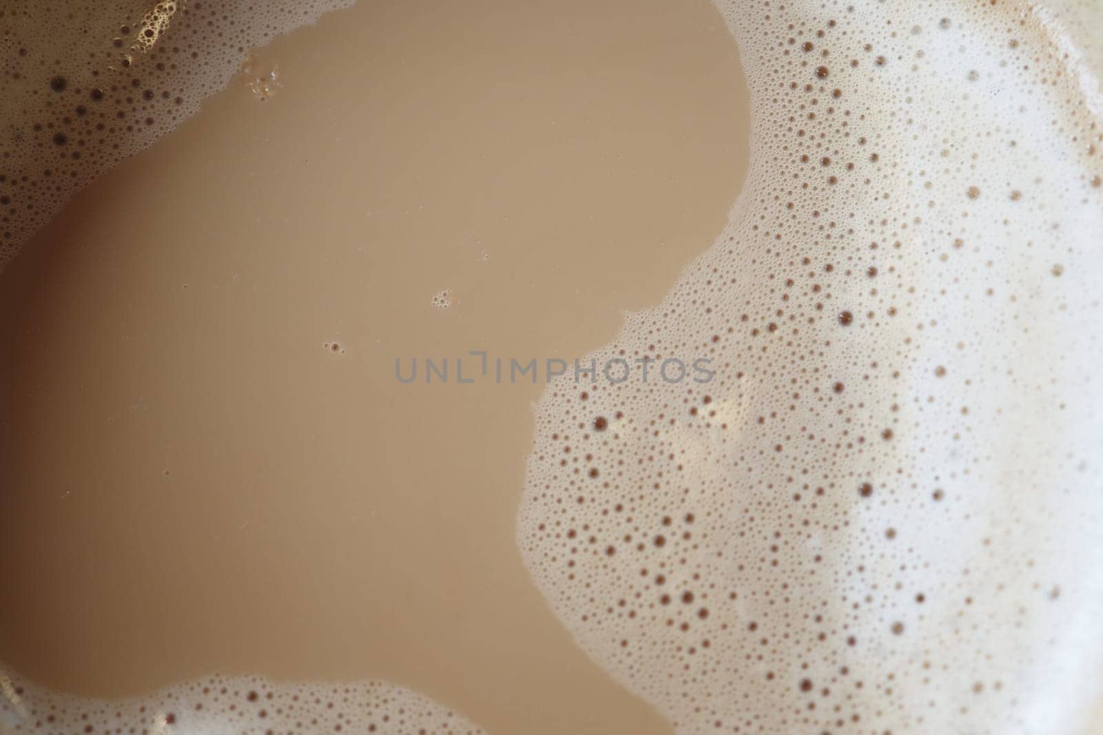 Creamy cappuccino foam fills the cup, showcasing rich textures and colors. The warm ambiance of the cafe enhances the comforting atmosphere perfect for relaxation.