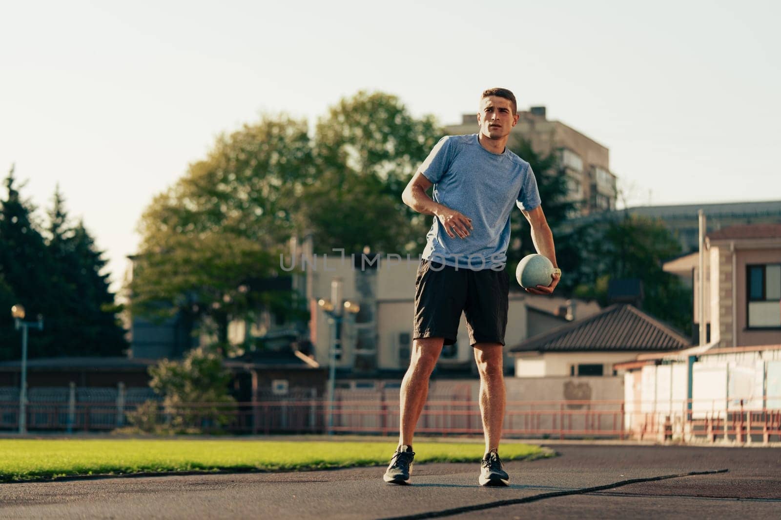 A young athlete stands on an outdoor field, focused on improving his ball control. The sun shines bright in a clear sky over a city background, creating a vibrant atmosphere for training.