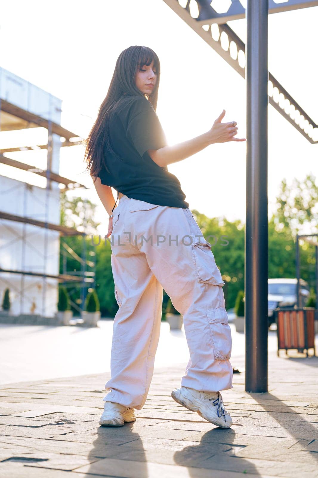 A young dancer performs in an urban area, dressed in casual attire with cargo pants and sneakers. The golden light of sunset highlights her movements, creating a dynamic atmosphere.