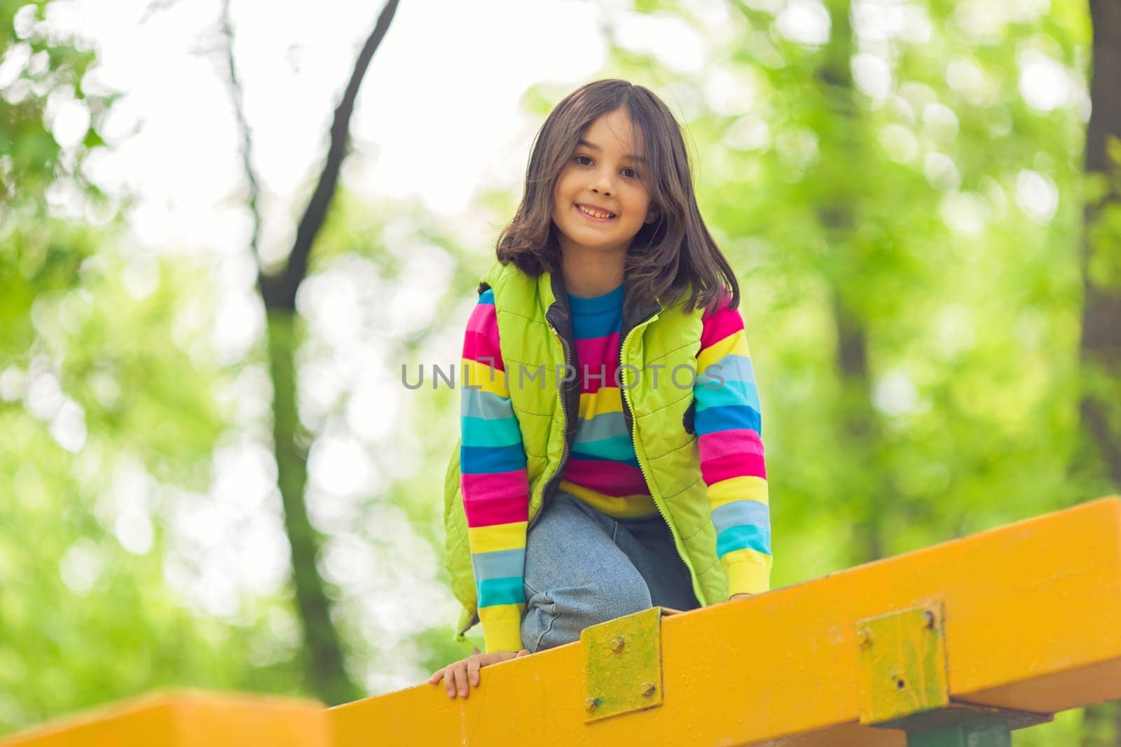 Portrait of a cute smiling little girl on a bright wooden platform in the park in spring